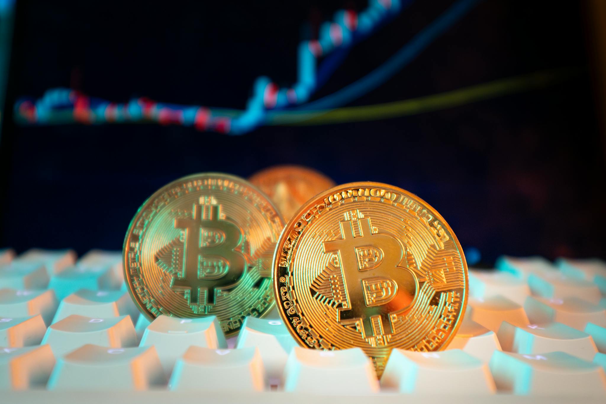 Golden Bitcoin coins on a keyboard with a financial chart in the background, representing digital currency and market trends.